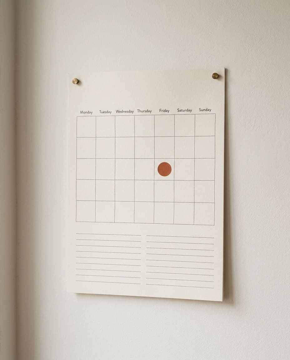 A blank paper wall calendar with a single rust dot on one day